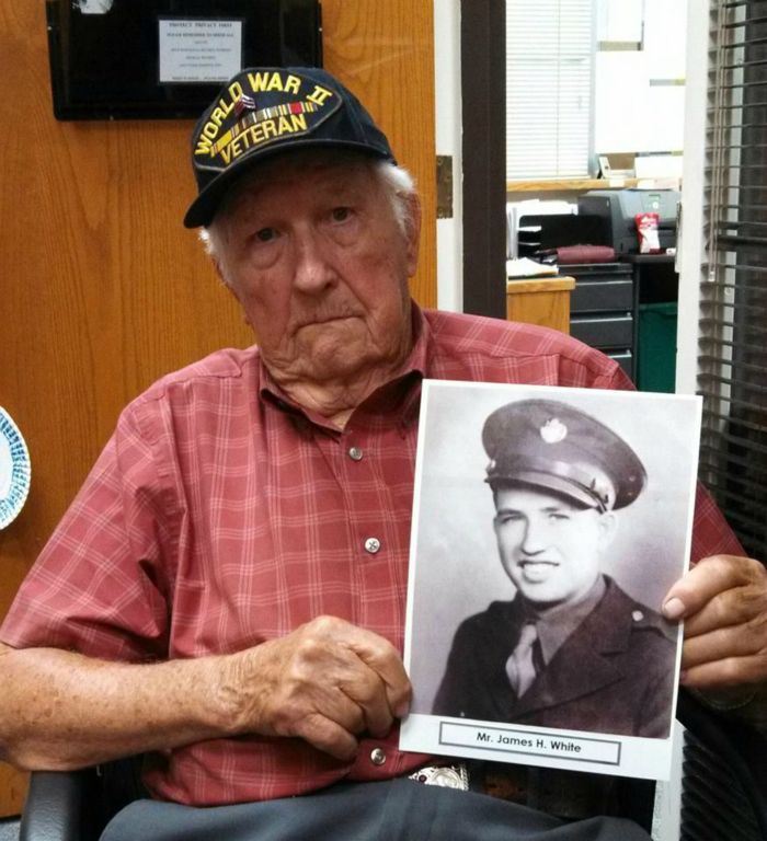 Man wearing World War II hat holds black and white image of James White